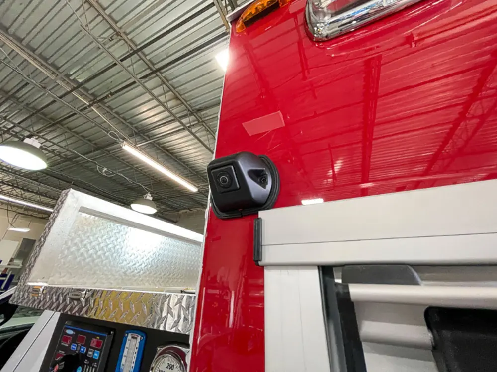 Exterior view of small fire truck showing cab, body compartments, and wheel/tire area.
